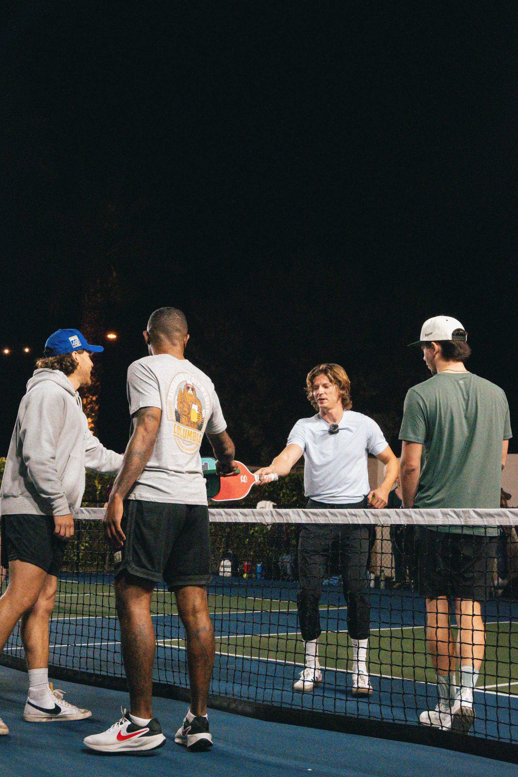Pickleball players meeting at the net during an evening game